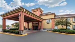 A hotel entrance with a covered area, a parking lot, and a building with a yellow facade and red accents. - Quality Inn & Suites Brownsburg - Indianapolis West (Brownsburg)