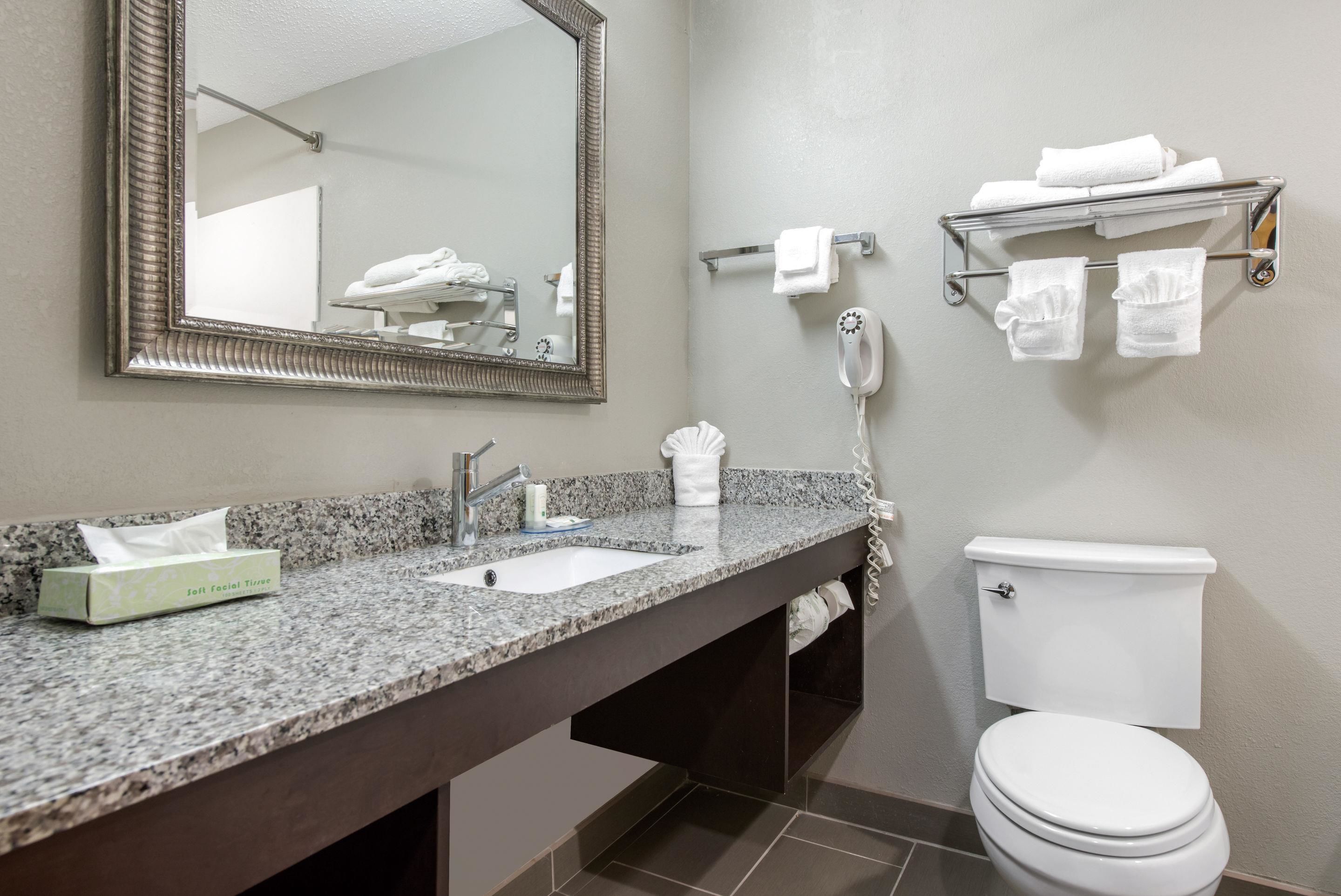A bathroom with a granite countertop, two sinks, a toilet, a mirror, a towel rack, and a phone.