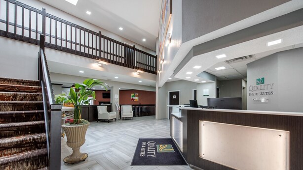 A hotel reception area with a double staircase, a reception desk, and a reception area with a sign reading "Quality". - Quality Inn & Suites Brownsburg - Indianapolis West (Brownsburg)