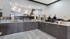 A modern kitchen with dark wood cabinets, a white countertop, and various appliances including a coffee machine and waffle maker. - Quality Inn & Suites Brownsburg - Indianapolis West (Brownsburg)