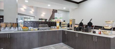 A modern kitchen with dark wood cabinets, a white countertop, and various appliances including a coffee machine and waffle maker.