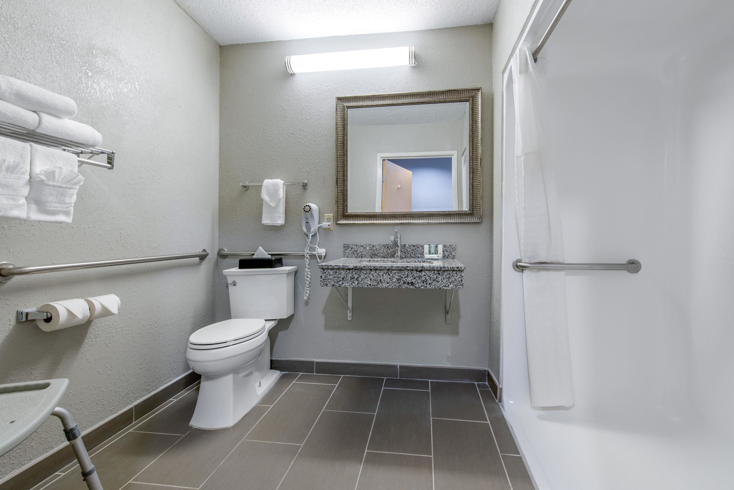 A bathroom with a toilet, sink, and shower. There are towels on a rack and a mirror above the sink.