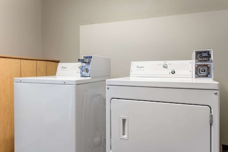 Two white Whirlpool washing machines in a laundry room with a wooden cabinet and a plain wall.