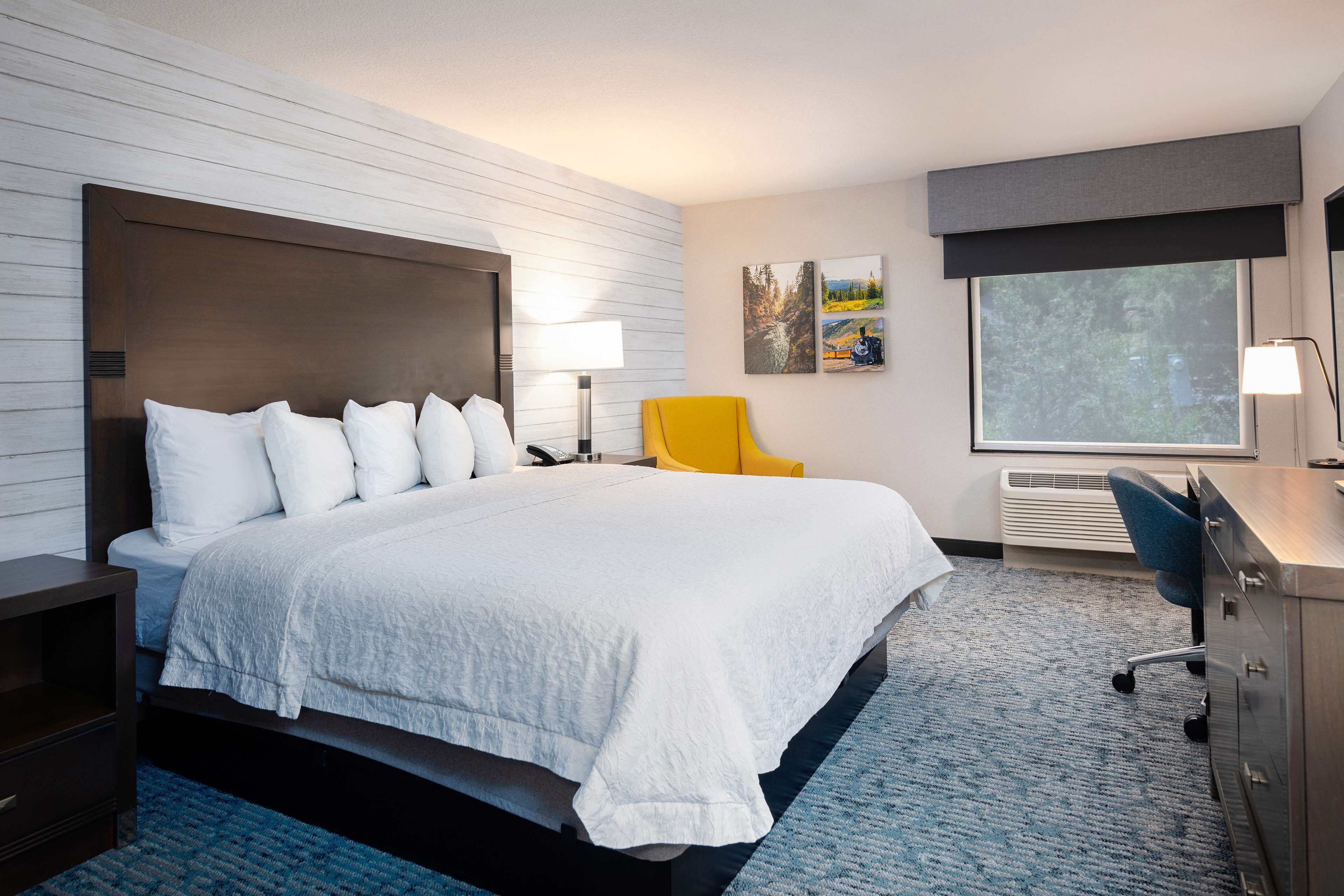 Une chambre d’hôtel avec un grand lit, un bureau, une chaise, une lampe et une fenêtre.