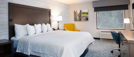 Une chambre d’hôtel avec un grand lit, un bureau, une chaise, une lampe et une fenêtre.