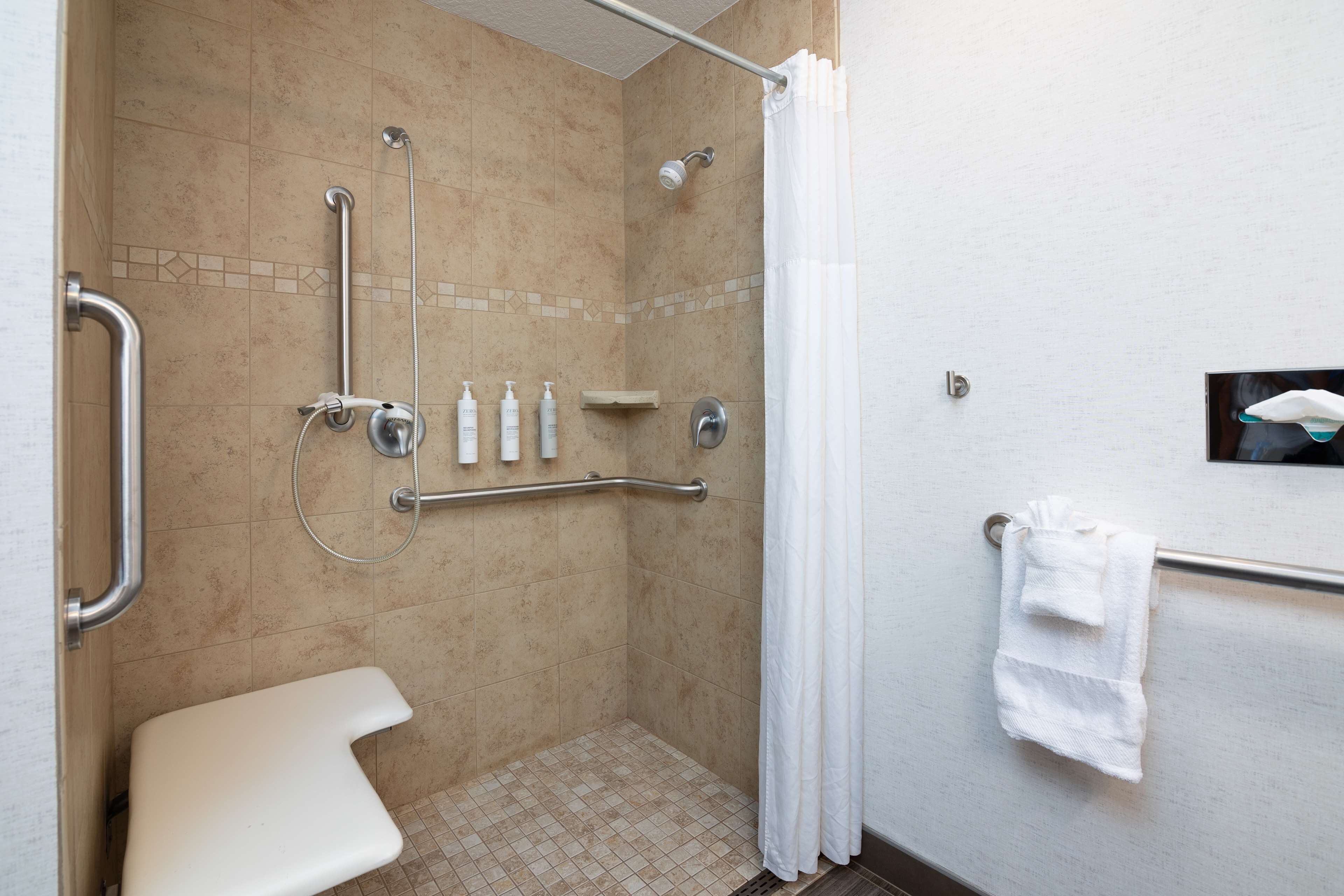 Une salle de bain moderne dotée d’une douche à l’italienne, de barres d’appui, de toilettes et d’un porte-serviettes.