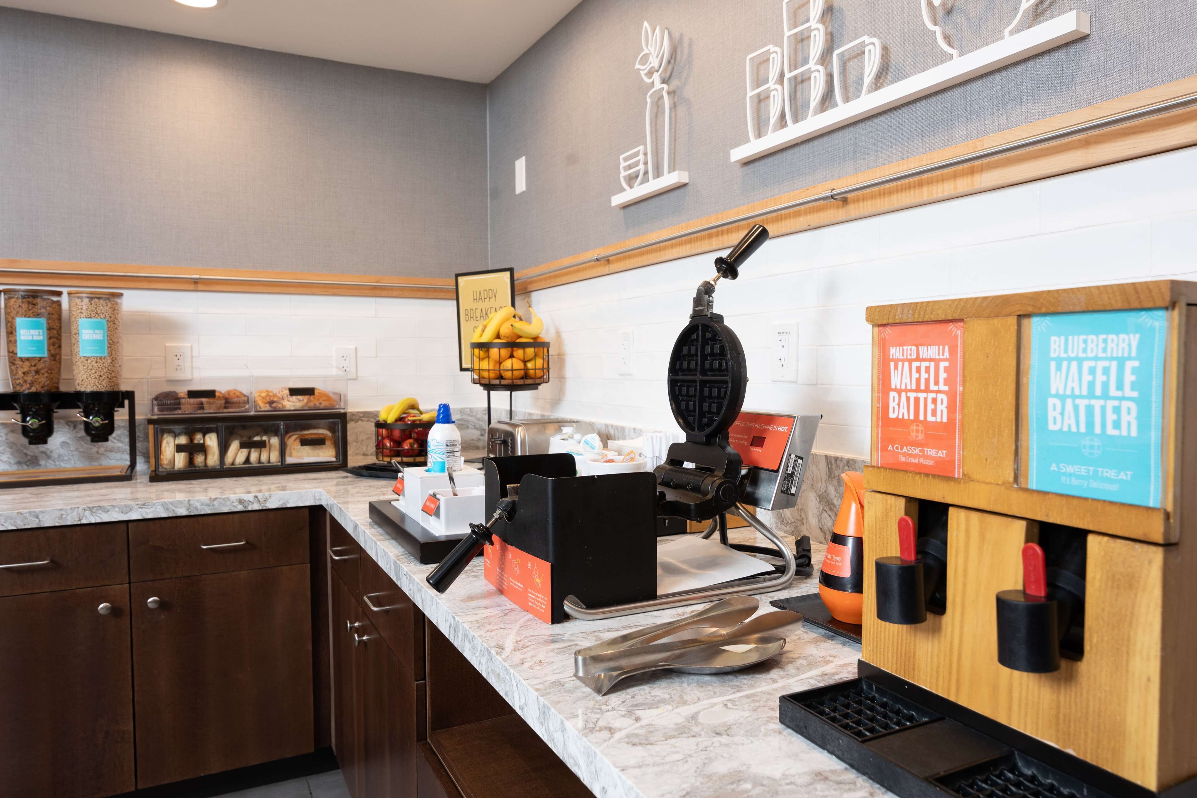 A modern kitchen with a waffle maker, waffle batter dispensers, and a fruit basket.