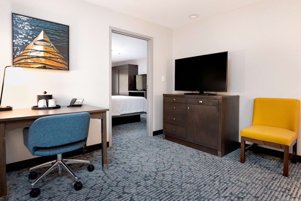 A hotel room with a bed, a desk with a chair, a television, a cabinet, and a painting on the wall.
