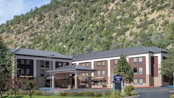 A modern hotel with a covered entrance, a sign indicating it is a Hampton Inn, and a mountainous backdrop.