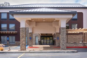 A modern building with a covered entrance, stone pillars, and a parking lot.