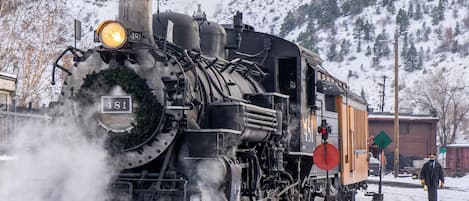 Een stoomlocomotief met het nummer 481 op een besneeuwd spoor, een persoon in de buurt en een gebouw op de achtergrond.