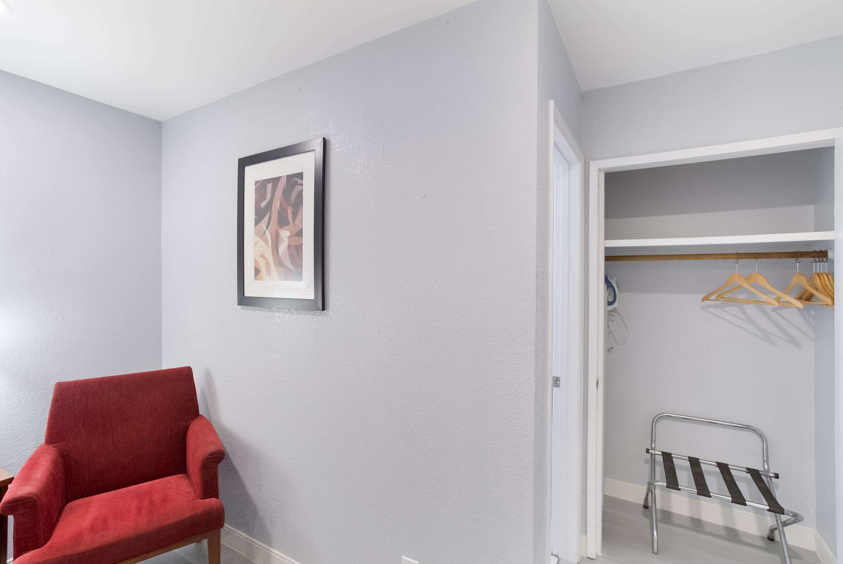 A room with a red chair, a framed picture on the wall, and a walk-in closet with hanging clothes.