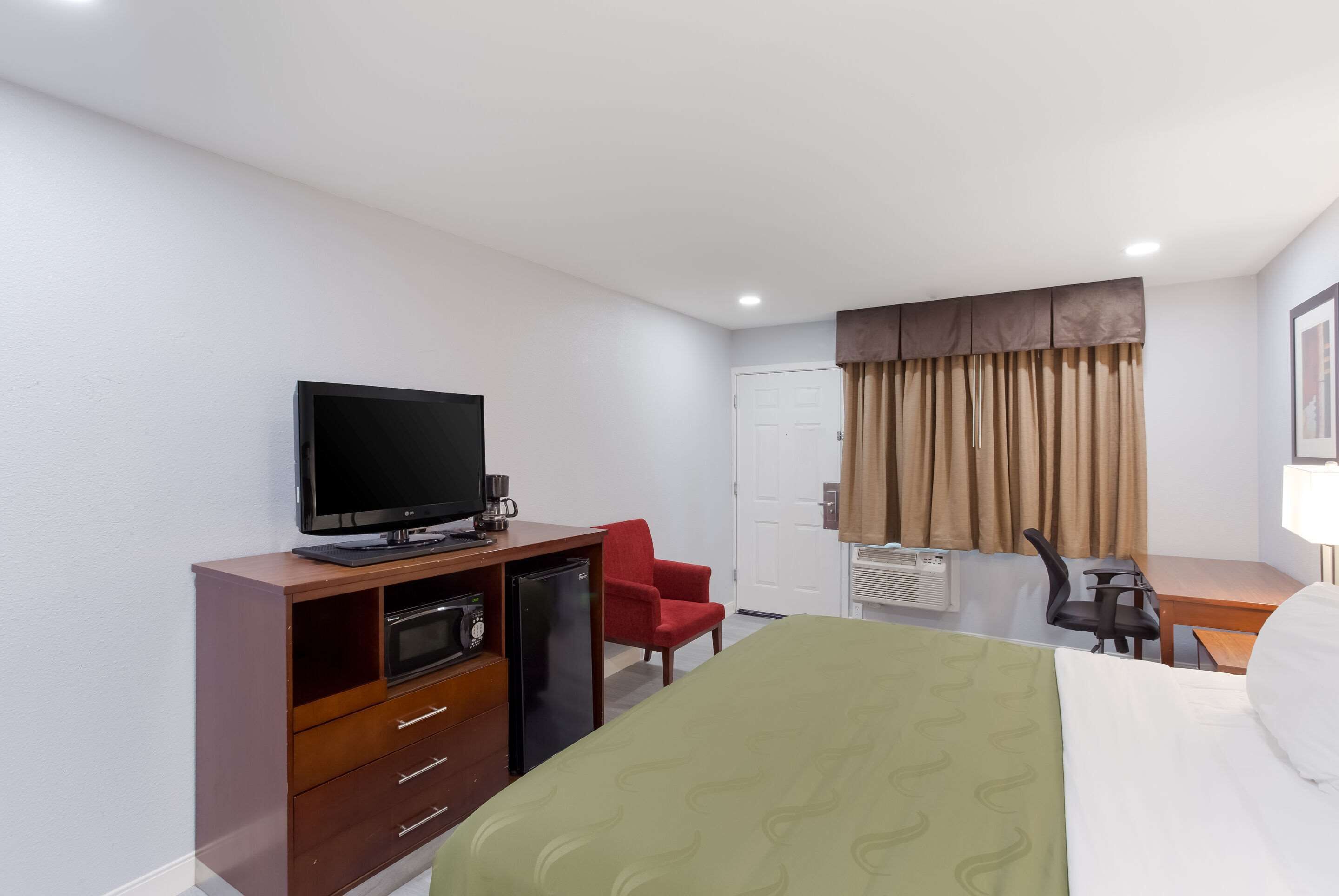 A hotel room with a bed, a desk, a chair, a television, a refrigerator, and a wardrobe.