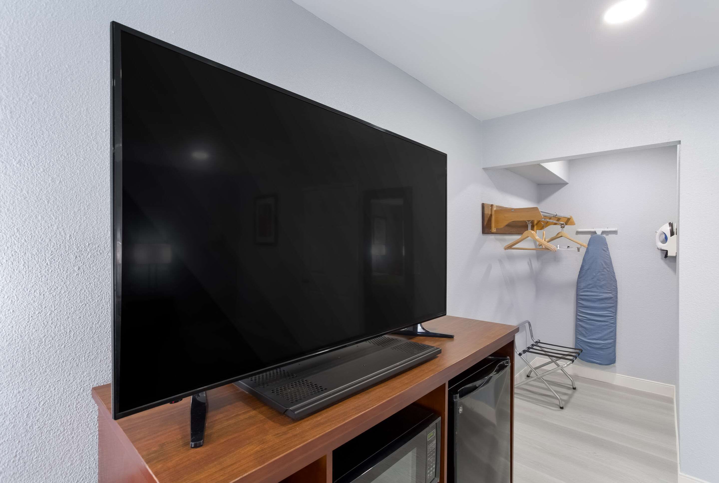 Een moderne woonkamer met een grote flatscreen televisie bevestigd aan een houten standaard, een compacte magnetron en een klein wasrek.