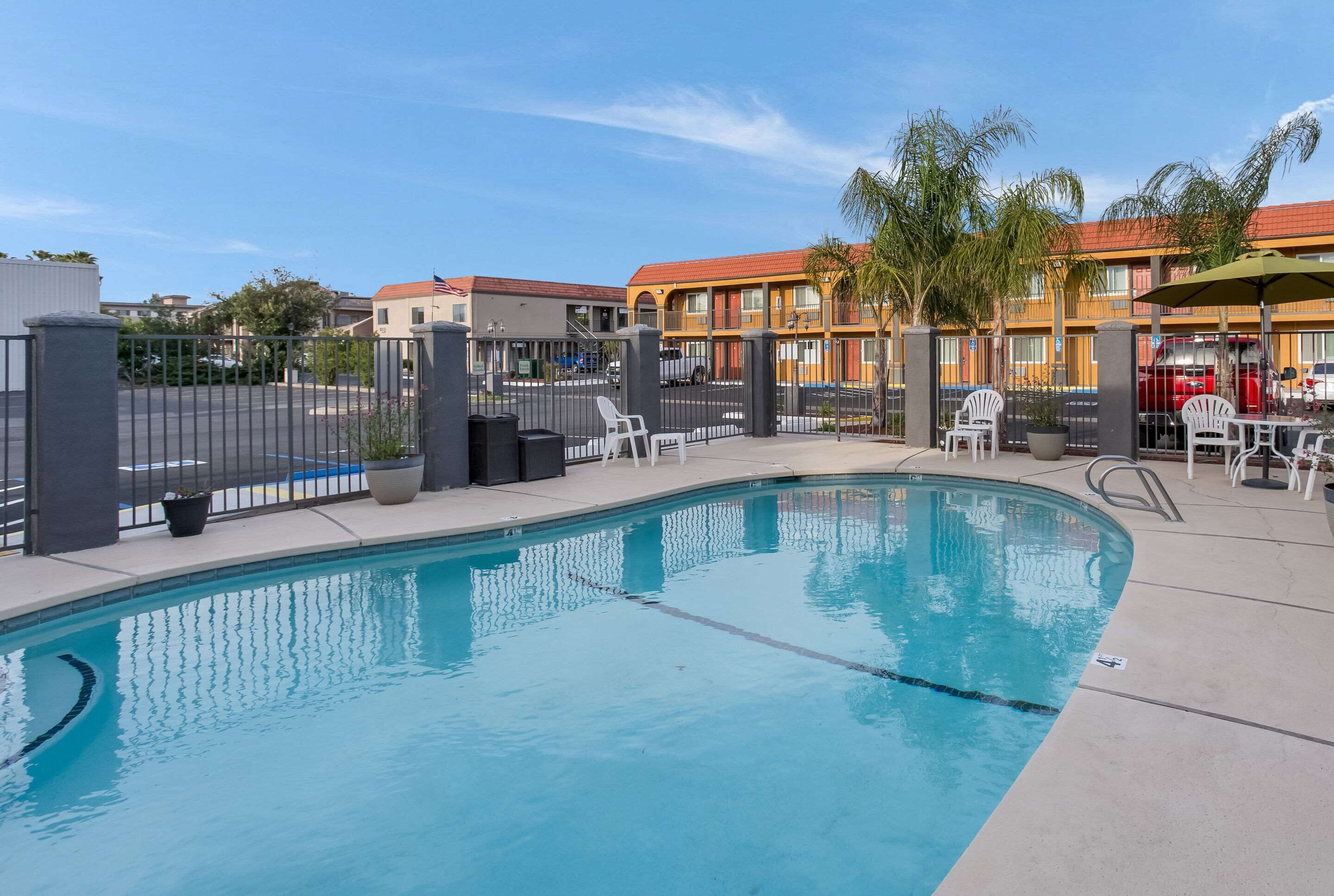 A swimming pool with a fenced area, outdoor seating, and a view of hotel buildings in the background.