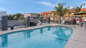 A swimming pool with a fenced area, outdoor seating, and a view of hotel buildings in the background.