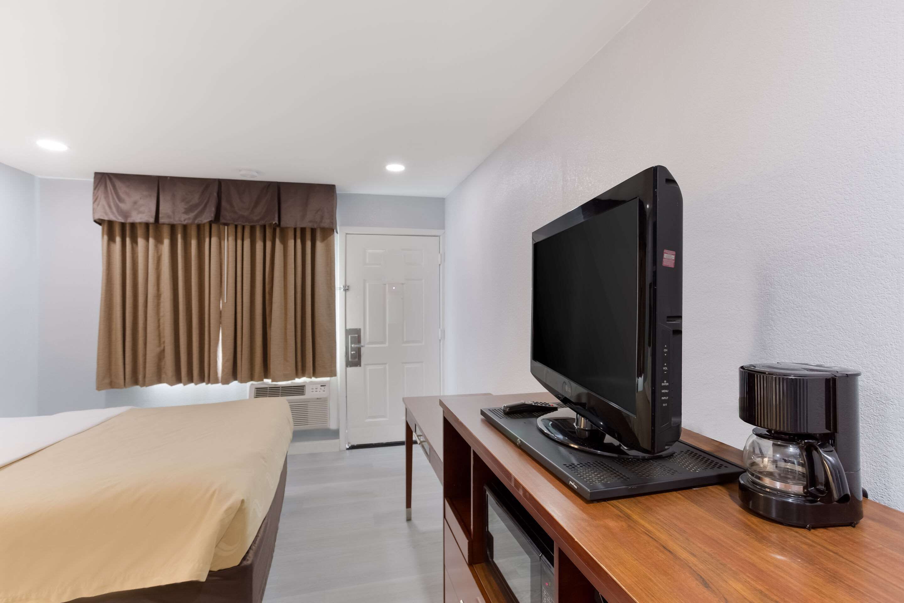 Una habitación de hotel con una cama, un televisor sobre un atril de madera y una cafetera.