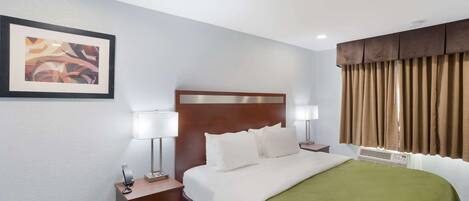 Habitación de hotel con cama, mesitas de noche, lámpara, un cuadro enmarcado y una ventana con cortinas.