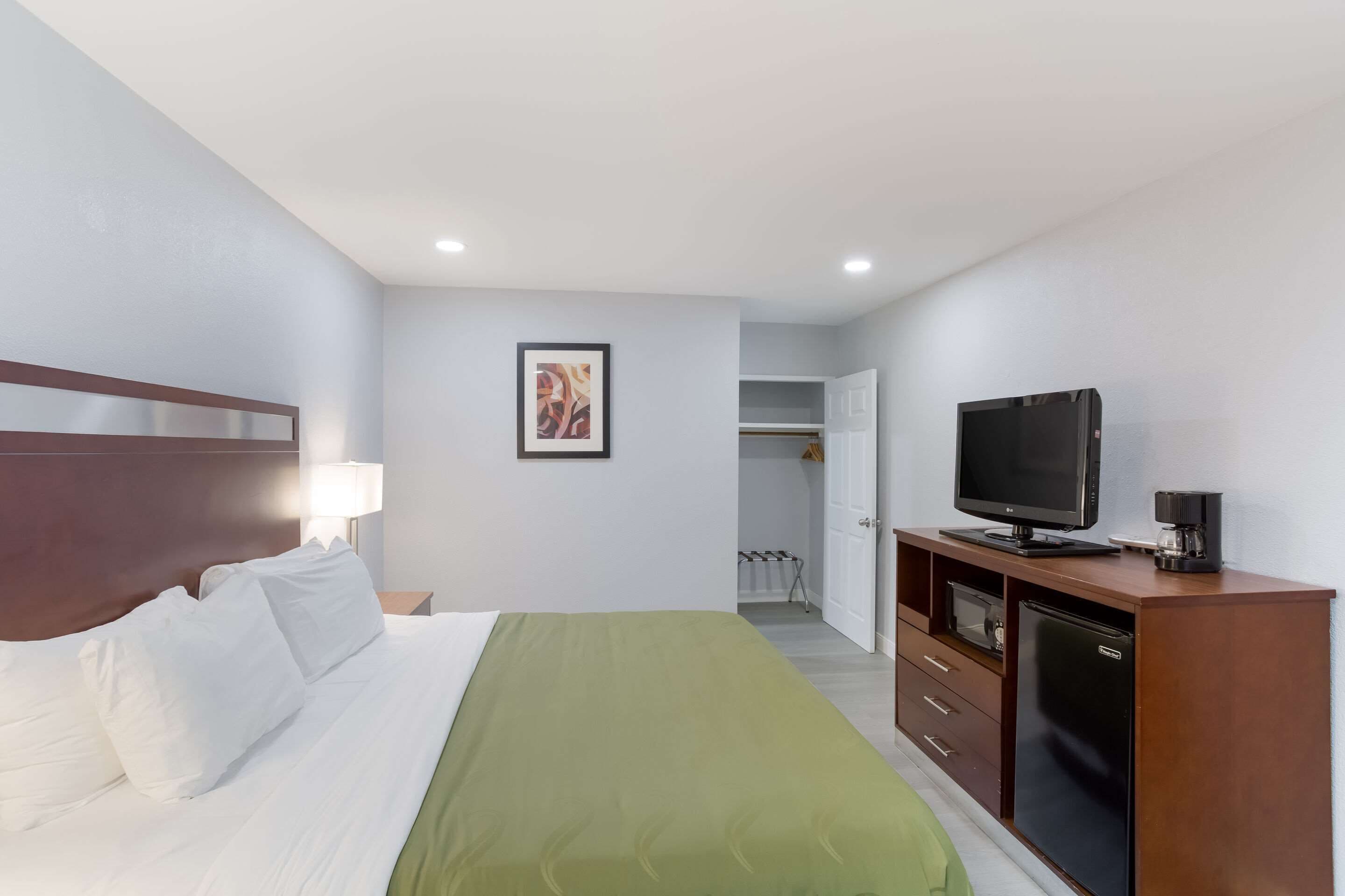 Una habitación de hotel con una cama, televisión, cafetera y armario.