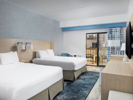 Habitación de hotel con dos camas, un escritorio y vistas al exterior.