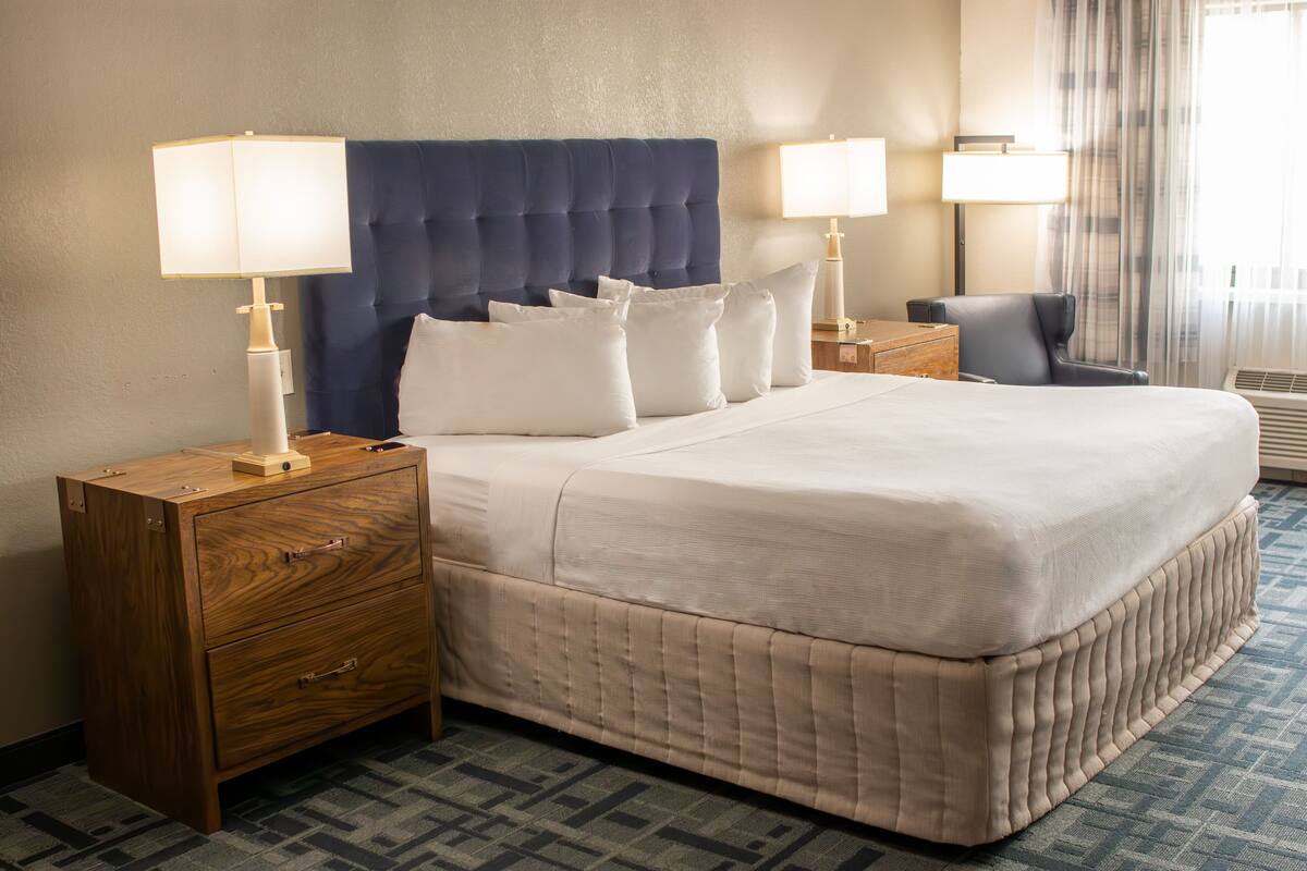 Ein Hotelzimmer mit einem großen Bett, zwei Nachttischen, einer Holzkommode und einem Sessel.
