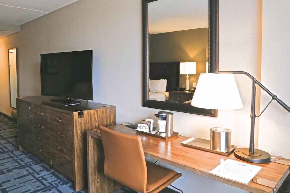 Une chambre d’hôtel avec un bureau en bois, une télévision, un miroir, une lampe et une chaise.