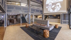 Un hall d’hôtel spacieux avec un plafond haut, un bar et un espace salon comprenant un canapé et des poufs.