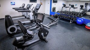 Une salle de sport équipée de tapis de course, de vélos elliptiques et d’une série de haltères.