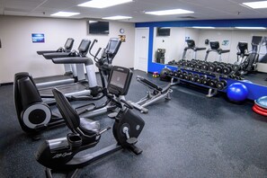 Ein Fitnessraum mit Laufbändern, Crosstrainern und einer Hantelbank.