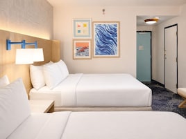 Habitación de hotel con dos camas, una mesita de noche, una lámpara de pared y obras de arte.
