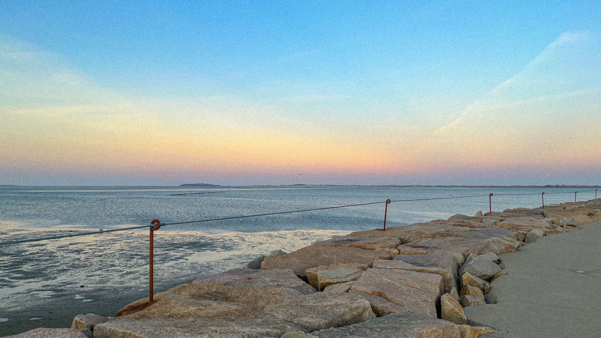 A coastal walkway with a rocky barrier and a rope fence.
