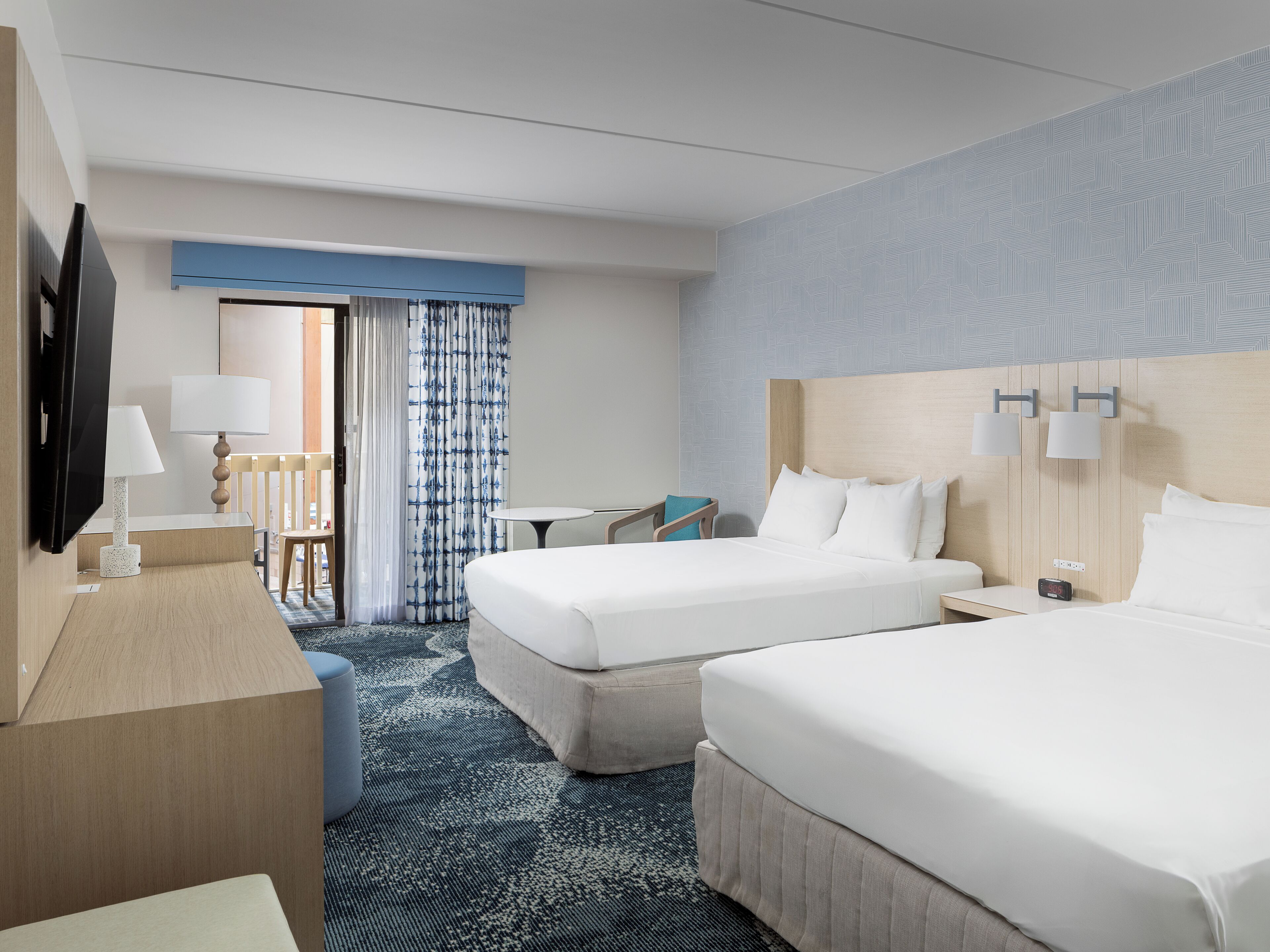 Une chambre d’hôtel avec deux lits, un bureau, une chaise, une télévision et une fenêtre avec des rideaux.
