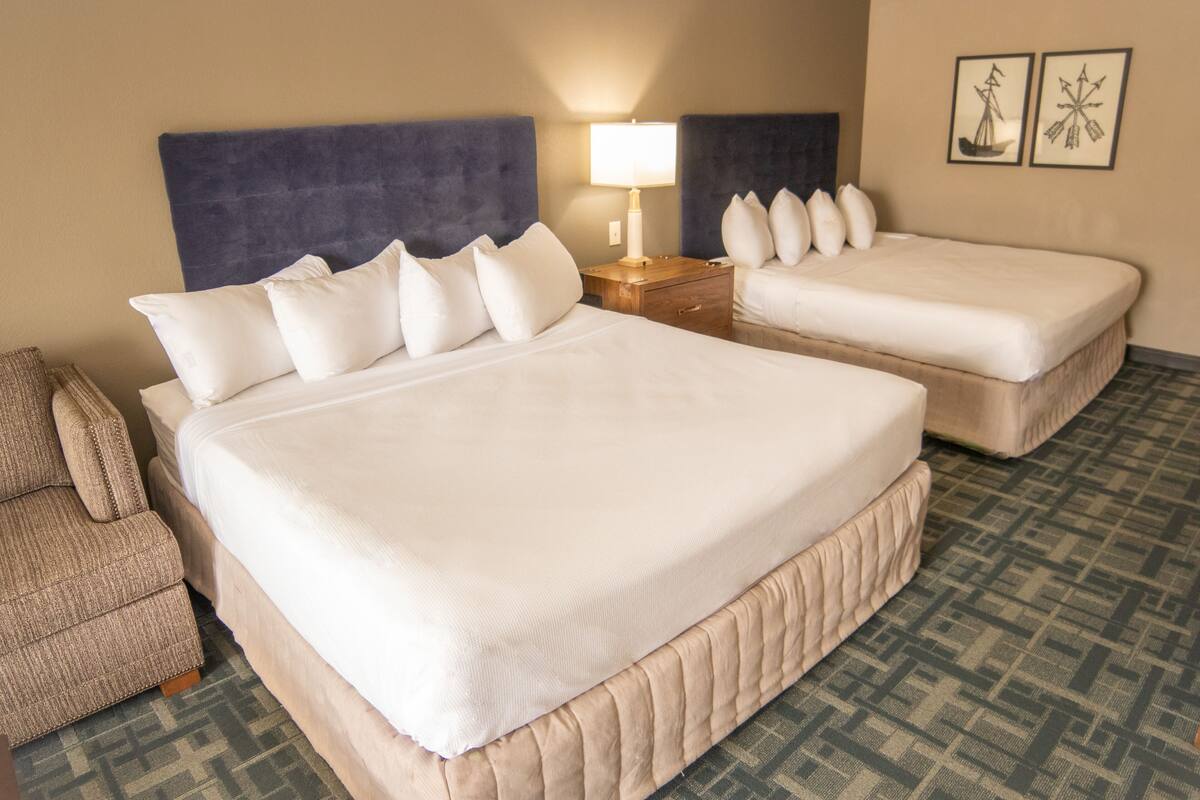 Une chambre d’hôtel avec deux lits, une table de chevet avec une lampe, une chaise et une moquette à motifs.