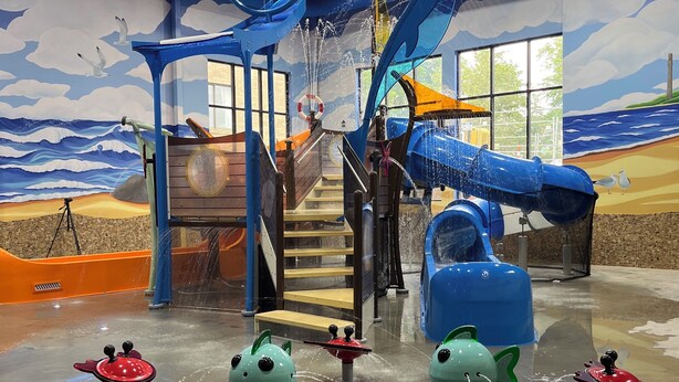 Un espace de jeux intérieur comprenant un toboggan, une structure d’escalade et des jeux d’eau.