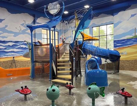 An indoor play area with a slide, climbing structure, and water play features.