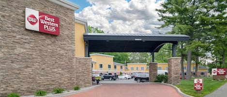 En entré till ett Best Western Plus-hotell med en fasad av tegel, ett takförsett parkeringsområde och en klar himmel.