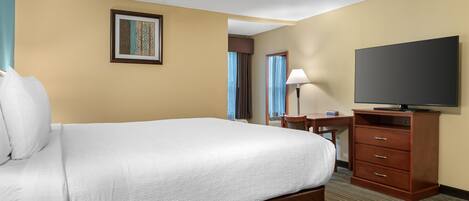 A hotel room with a large bed, a desk with a chair, a television, and a wardrobe.