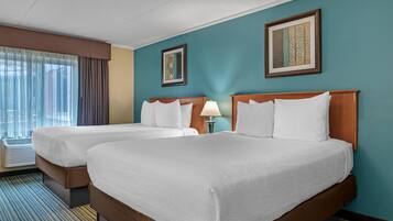 A hotel room with two beds, a window with curtains, and two framed pictures on the wall.