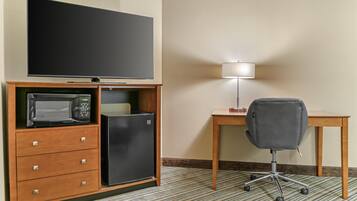 Habitación de hotel con televisión de pantalla plana, microondas, refrigerador pequeño, escritorio, silla y lámpara.