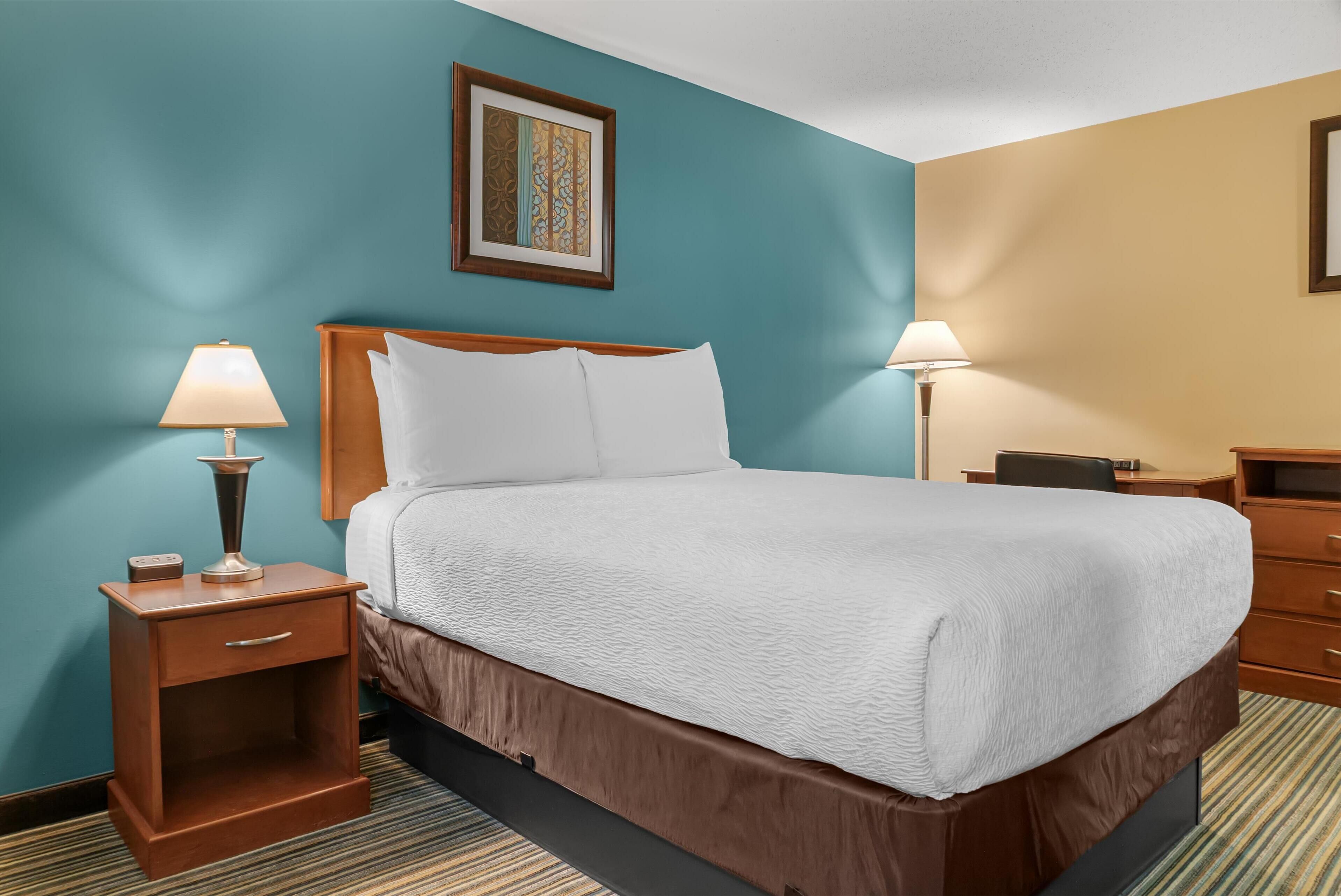 A hotel room with a bed, nightstands, and a framed picture on the wall.