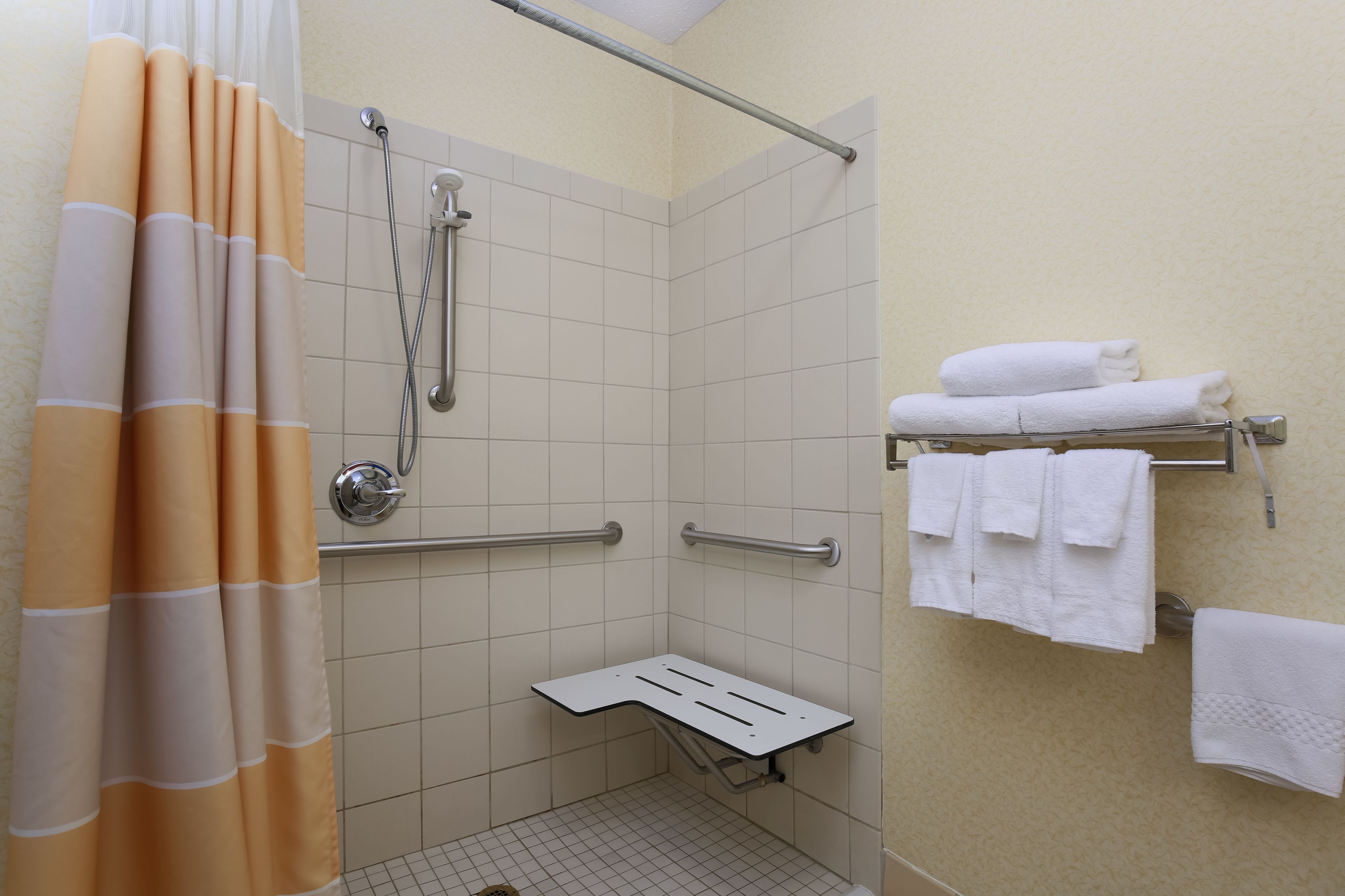 A shower area with a white tiled wall, a showerhead, a grab bar, and a towel rack with towels.