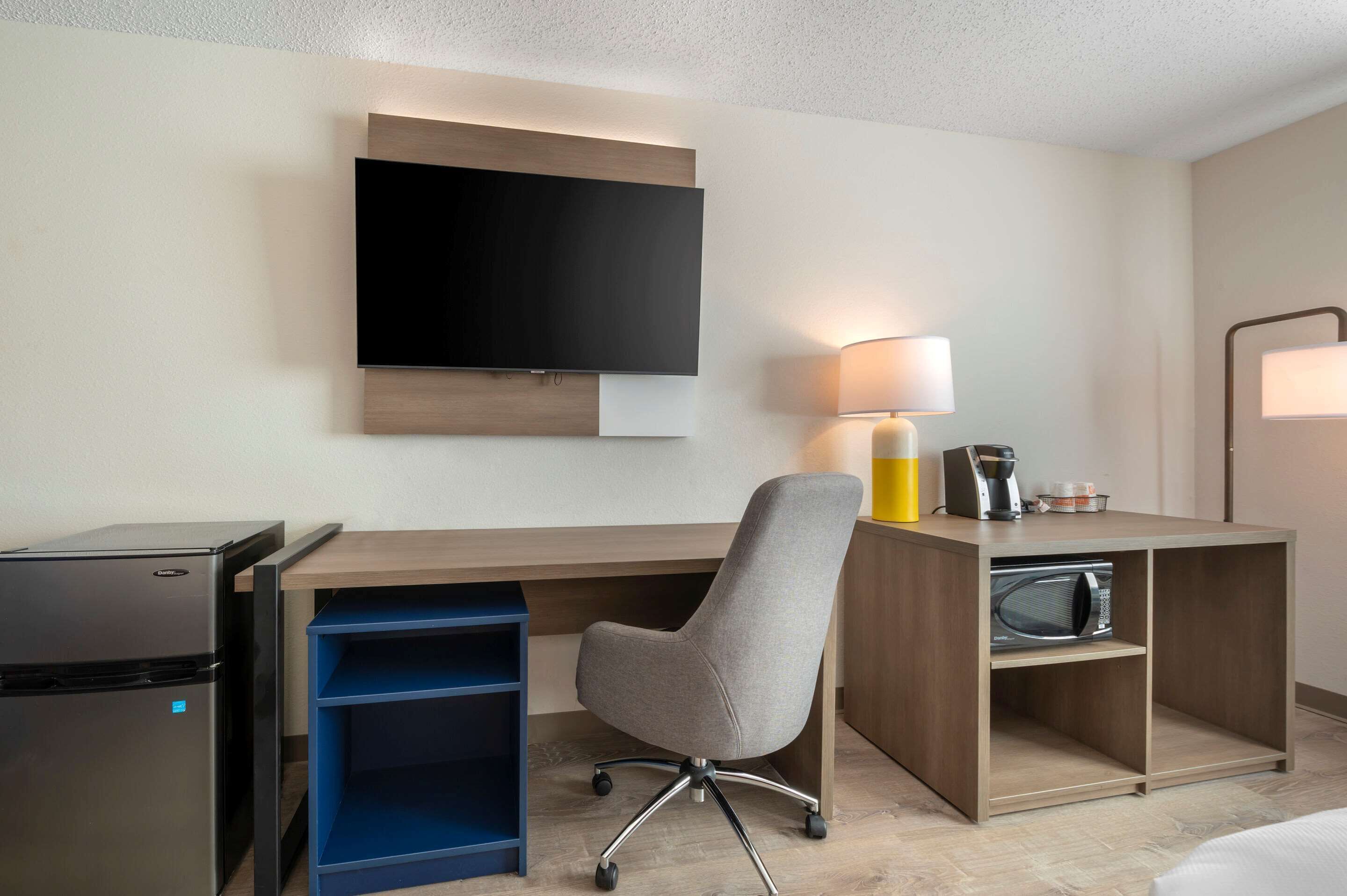 Une chambre d’hôtel équipée d’un téléviseur à écran plat fixé au mur, d’un bureau avec une lampe, d’un four à micro-ondes et d’un petit réfrigérateur.