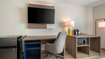 Une chambre d’hôtel équipée d’un téléviseur à écran plat fixé au mur, d’un bureau avec une lampe, d’un four à micro-ondes et d’un petit réfrigérateur.