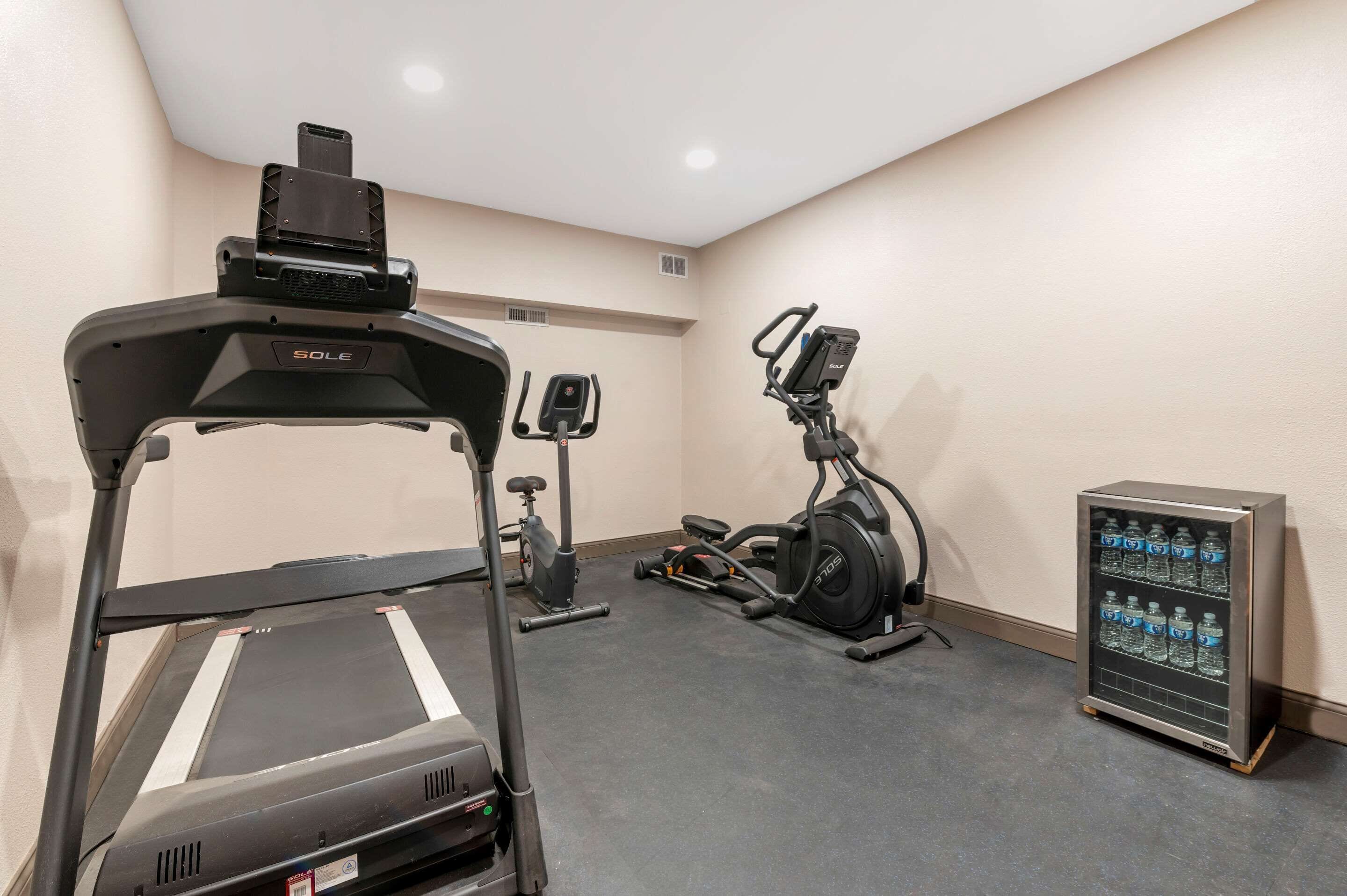 Un gimnasio con cinta de correr, elíptica y bicicleta estática, además de un dispensador de agua.