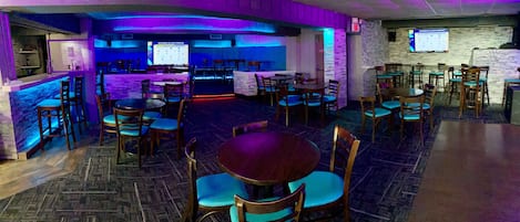 A restaurant with wooden tables and chairs, a bar area, and a projection screen displaying a menu.