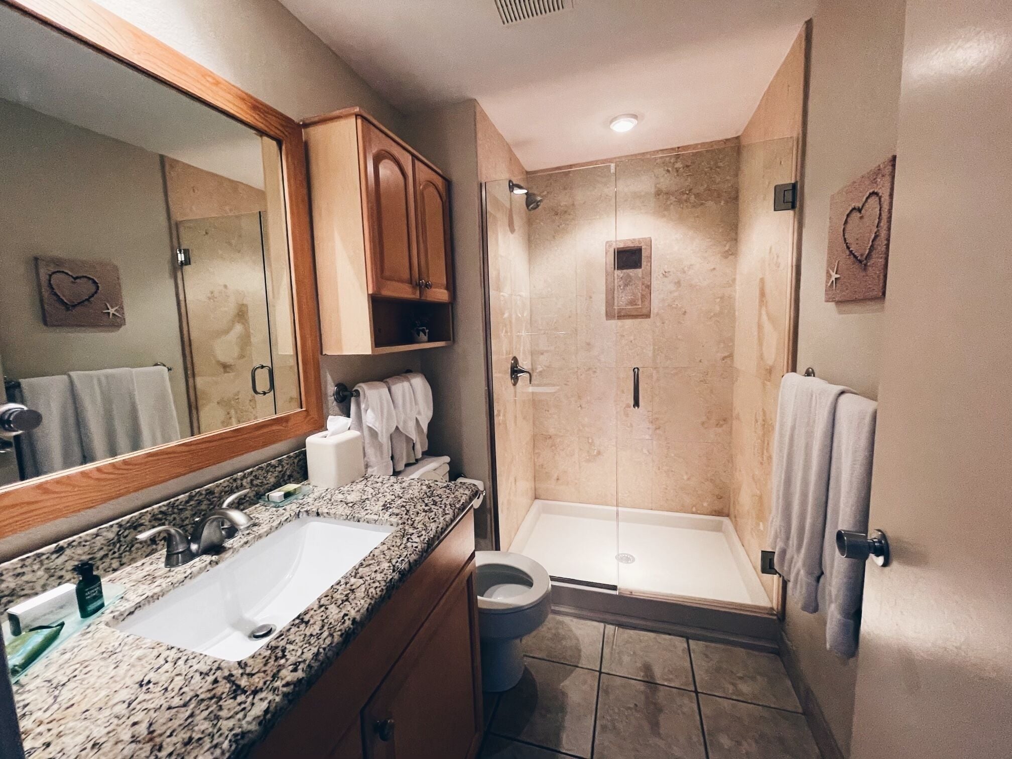 A bathroom with a sink, mirror, vanity, towel rack, shower, and toilet.