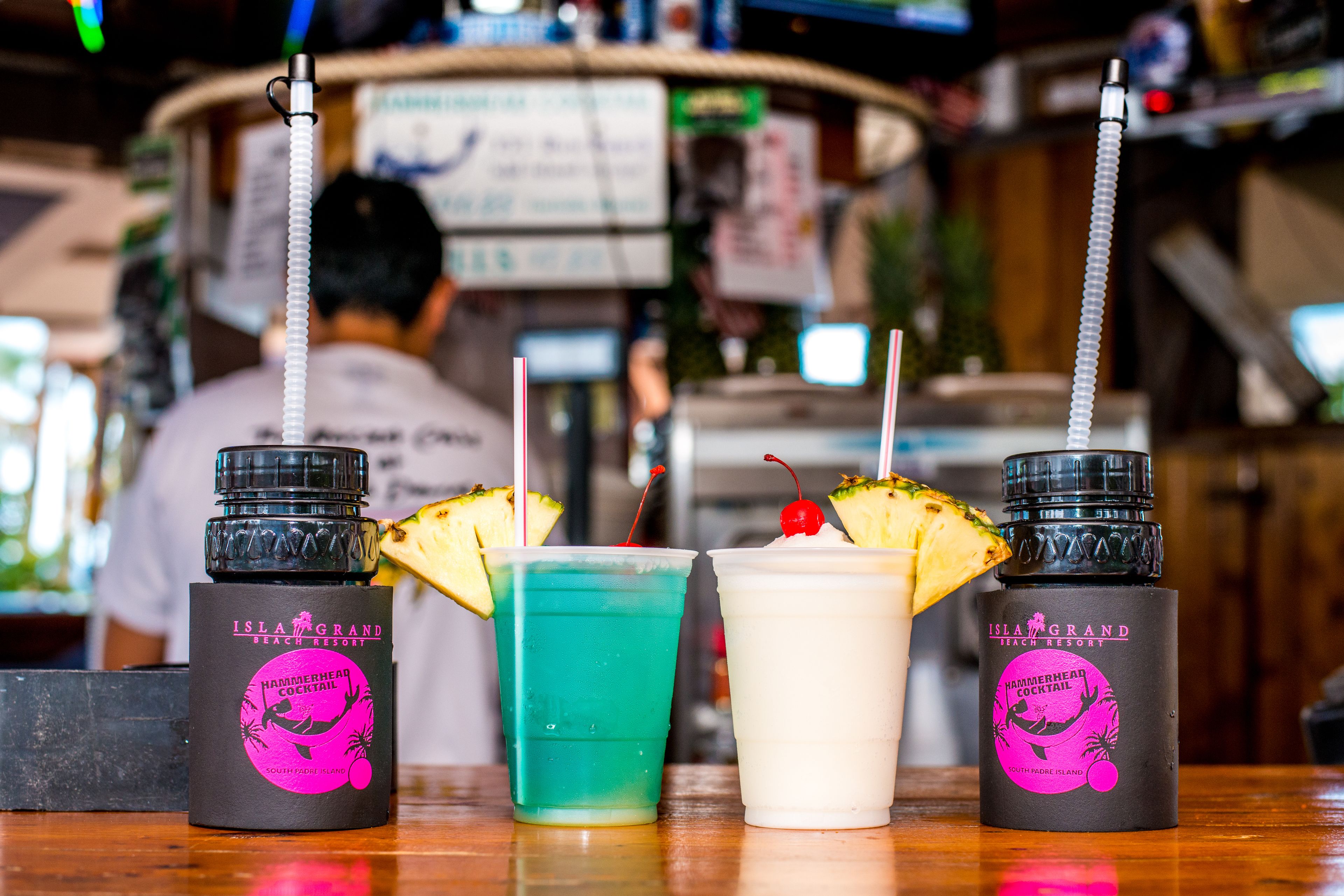 Three drinks with straws and pineapple garnishes on a bar counter.