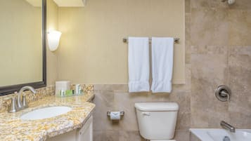 Un baño con lavamanos de encimera de granito, inodoro, bañera y toallero con dos toallas blancas.