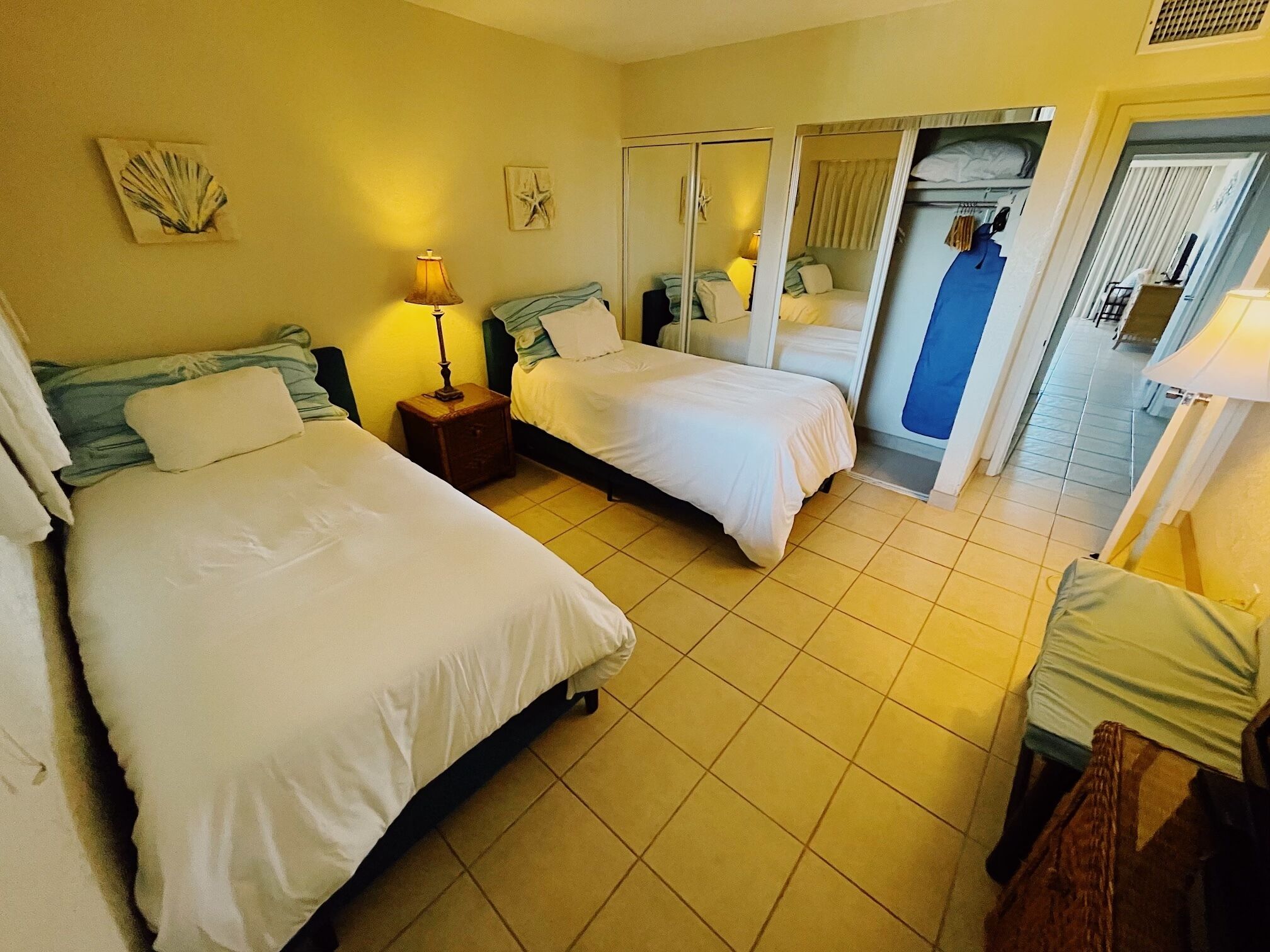 A hotel room with two beds, a nightstand with a lamp, a mirror, and a view of the hallway.