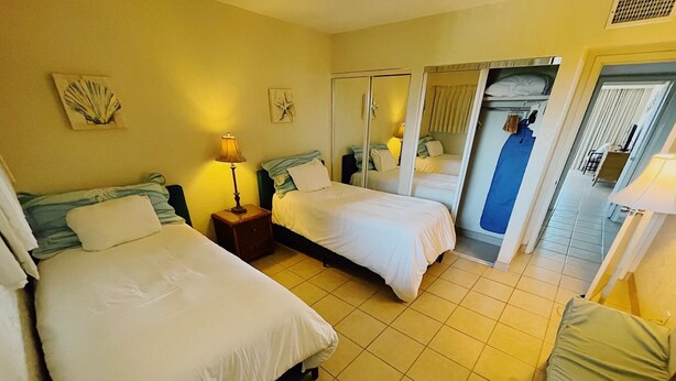 Habitación de hotel con dos camas, una mesita de noche con lámpara, un espejo y vista al pasillo.